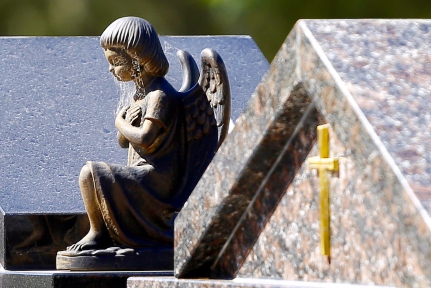 A small statuette of a weeping angel sits atop an unidentified gravestone in a cemetery.