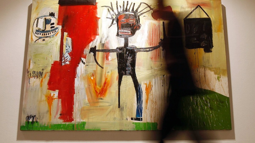 A man walks in front of a painting by Jean-Michelle Basquiat