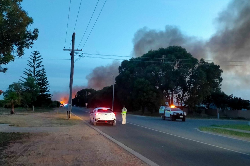 A dusk shot of a road blocked by police due to smoke and flames visible