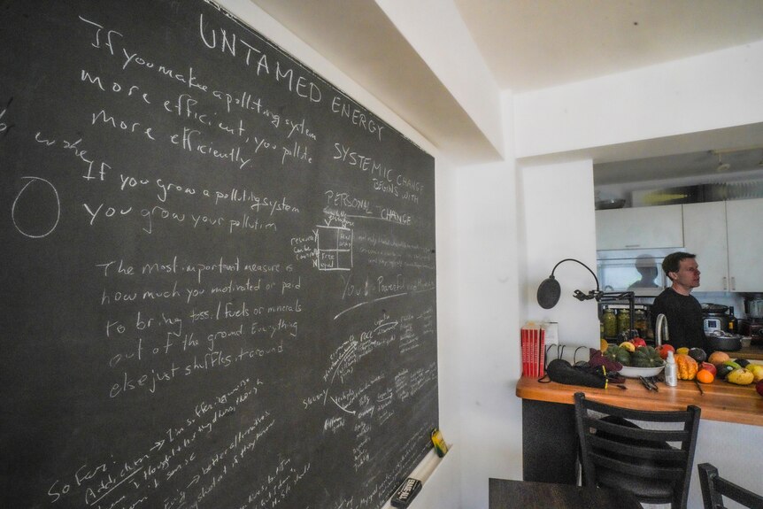 Josh Spodek in his kitchen near a blackboard with writing about energy and pollution on it