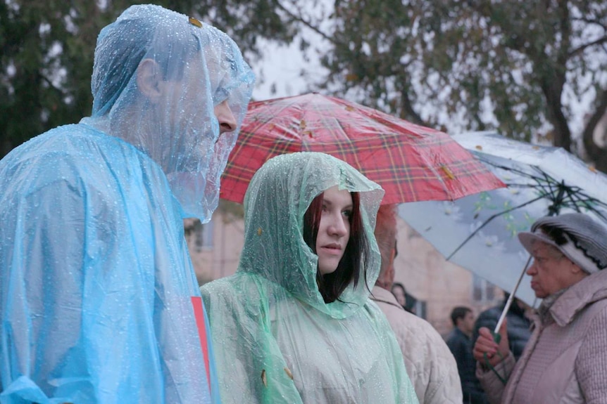 Supporters wearing plastic rain coats wait for the opposition leader