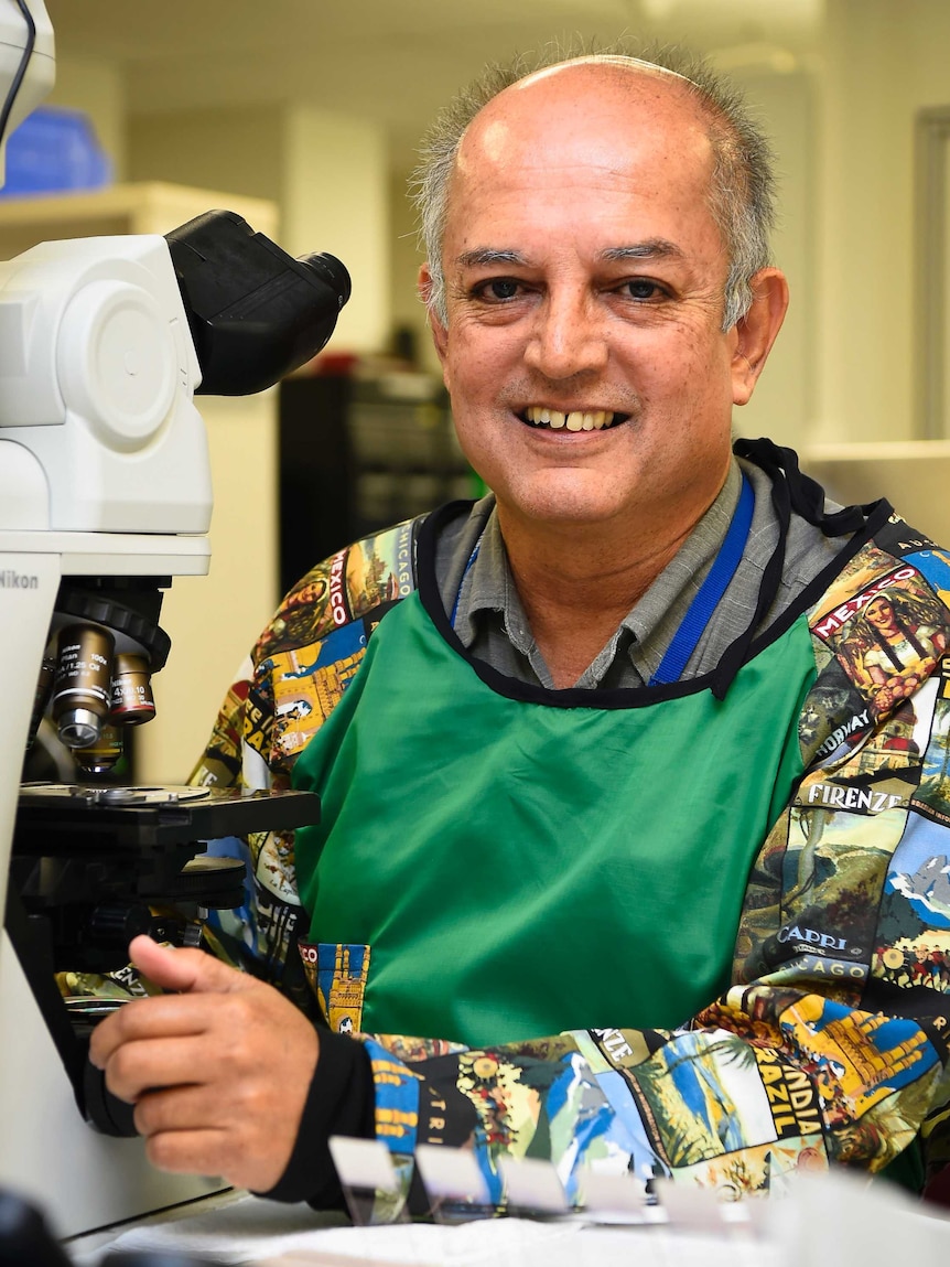 Professor Robert Norton sitting in front of a microscope with slides underneath, wearing a green apron