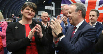 Arlene Foster applauds the result at Belfast North with a colleague in front of the union jack flag.