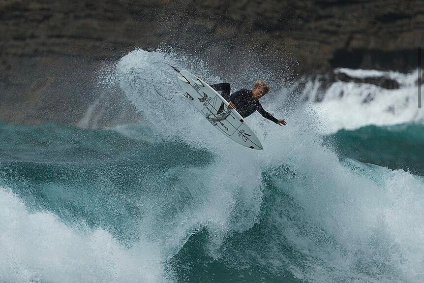 Manning doing an air on his surfboard above a large wave