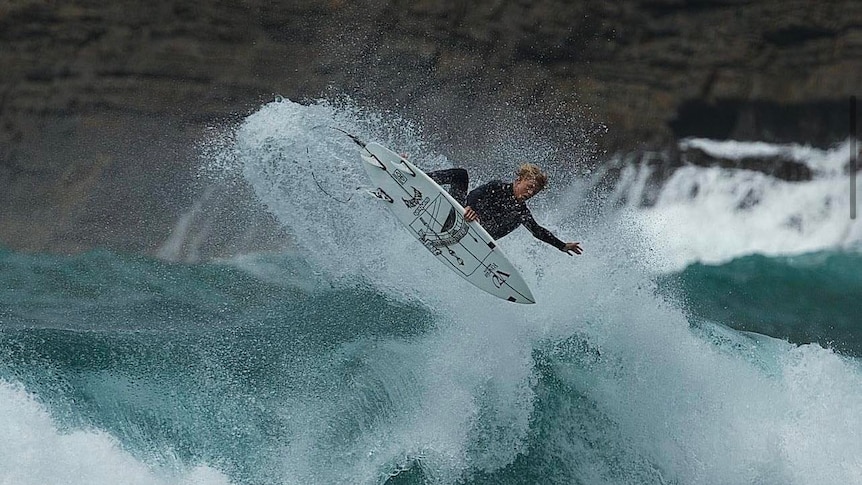 Manning doing an air on his surfboard above a large wave