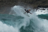 Manning doing an air on his surfboard above a large wave