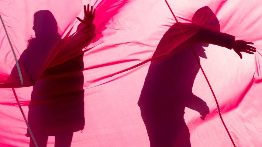 The shadows of a man and woman are cast against the pink fabric of the balloon as they help deflate it post-flight.