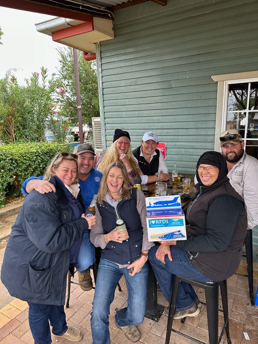 A bunch of people, very happy and smiling, gather around a table outside a pub in Windorah.