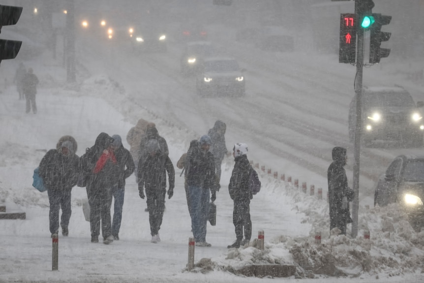 People walk down a street amid a snowfall.