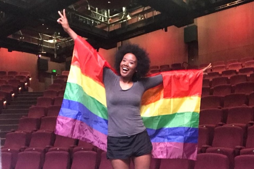 DJ, actor and presenter Faustina Agolley smiling and wearing a rainbow flag as a cape.