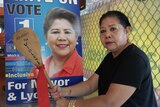 Woman holds a wooden spoon in front of a political corflute poster of her face