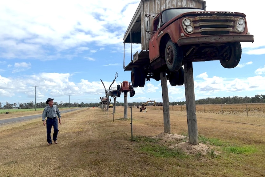 Elderly man walking beside a road, looking at a row of old vehicles on top of old power poles.