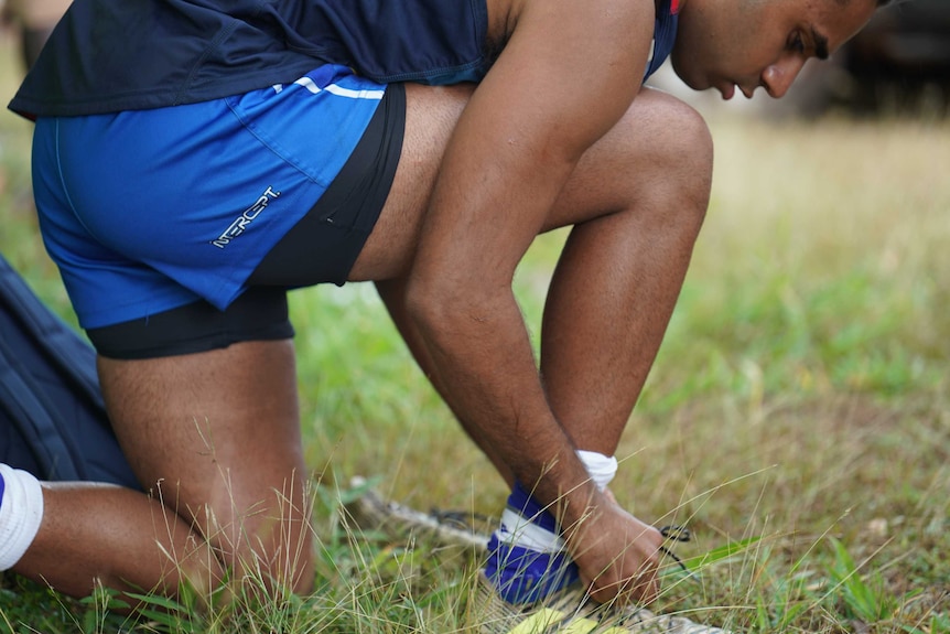 Michael bends over to lace up his football boots before a game in Yirrkala.