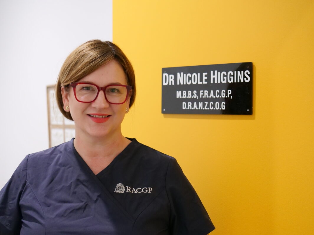 portrait shot of Dr Higgins standing in front of the door to her surgery with her name on the door