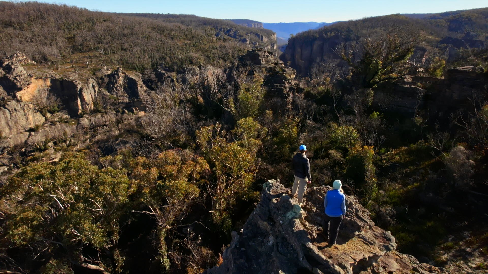 Two bush walkers stand on a rock formation in a canyon.