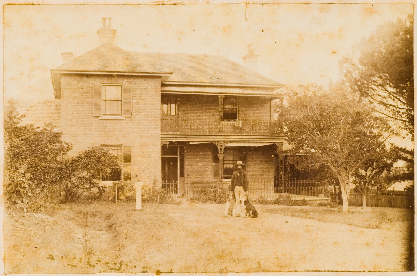 An archival sepia image of a man and a child standing out the front of a Victorian-style property in 1891.