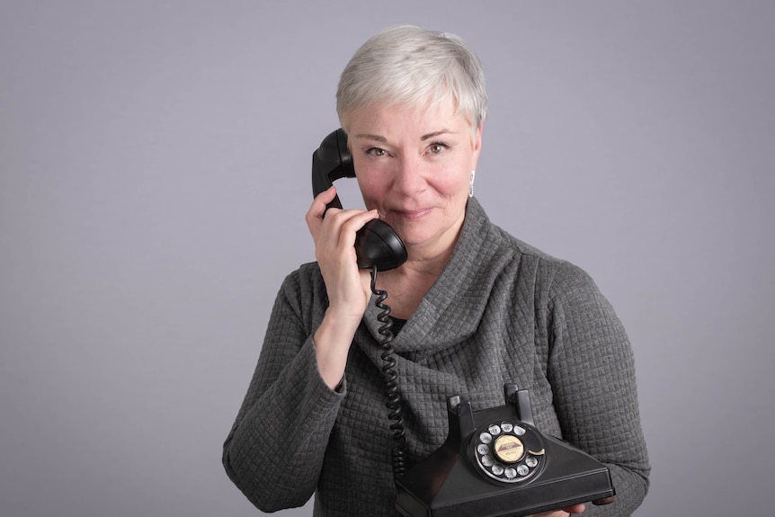 Mature aged lady with short grey hair holding a telephone receiver up to her ear