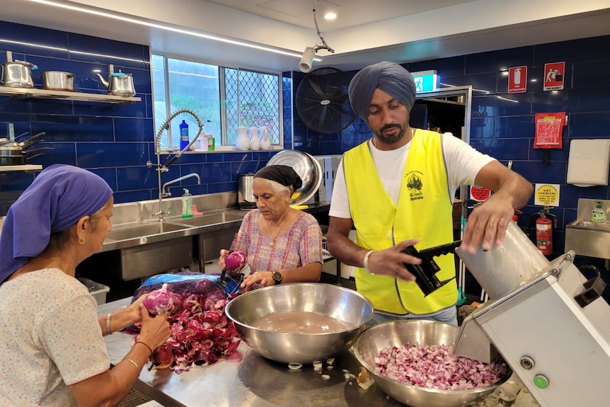 Three Sikhs cut onions in kitchen