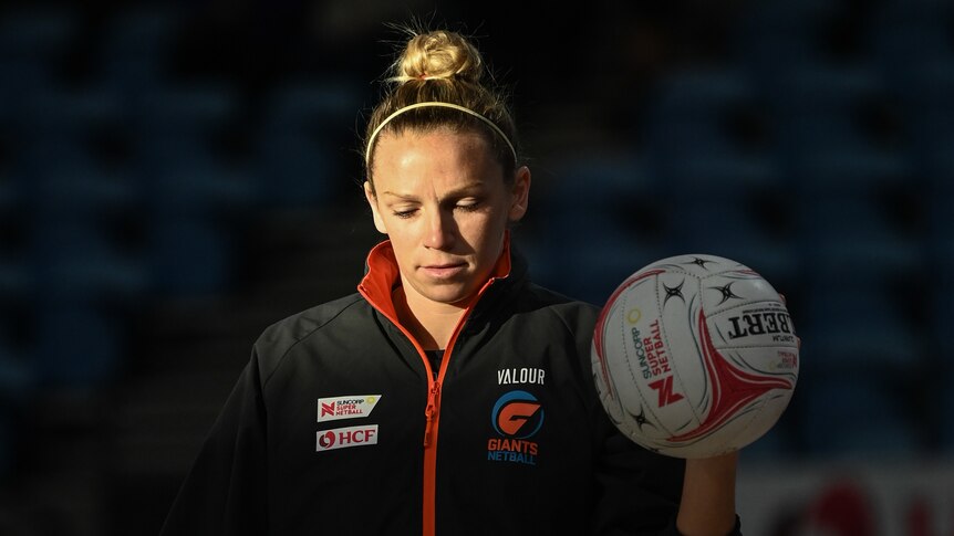 Jo Harten looks down and holds the ball in her left hand as sun floods half of her face in a dark stadium