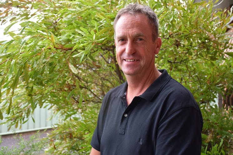 A man posing for a photograph in front of a bush.