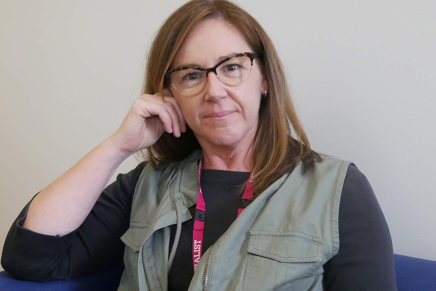 A middle-aged woman with her hand up against her cheek looks at the camera