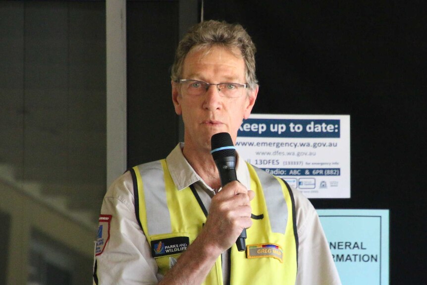 A man wearing a hi-vis vest and spectacles and talking into a microphone.