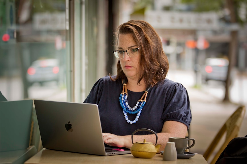 Julia Gilchrist works at a laptop computer at table on the sidewalk.