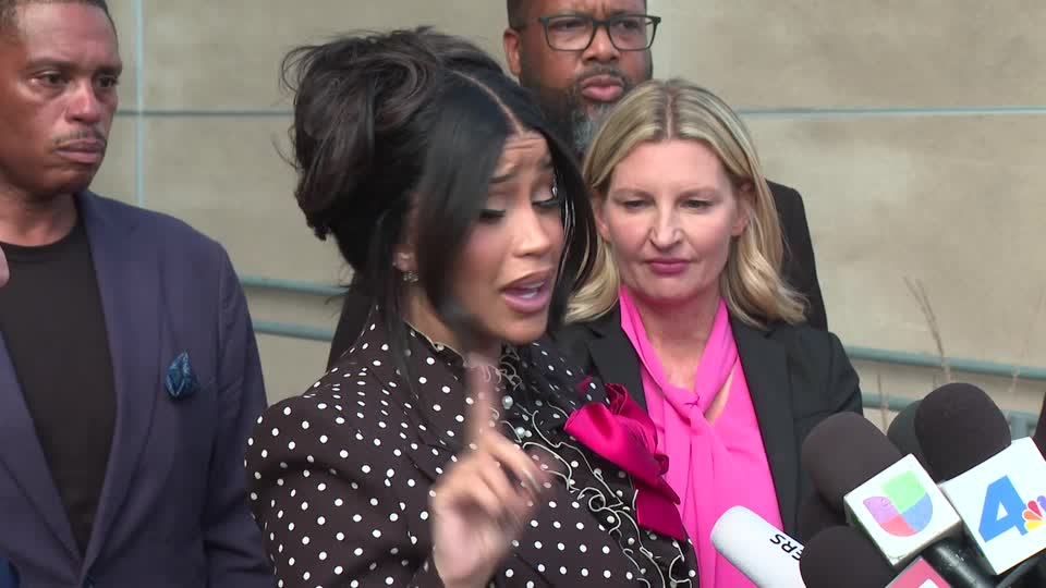 Cardi B speaking into microphones with her finger raised. 