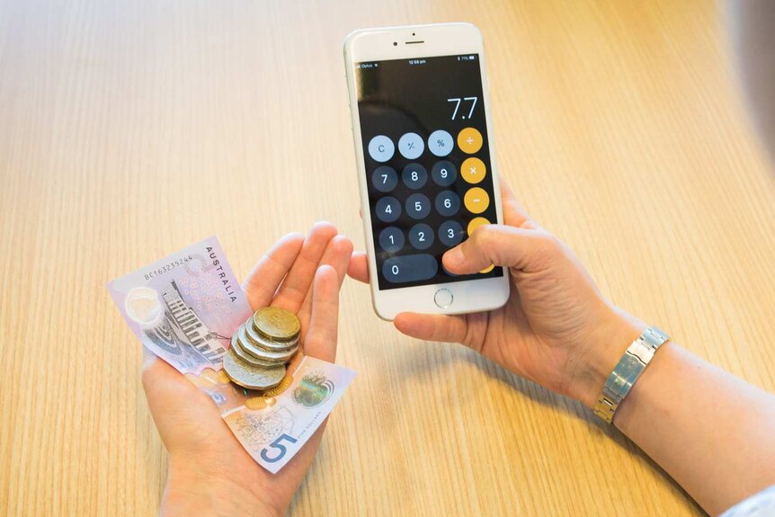 Woman holding a mobile phone and looking at money in her hand.