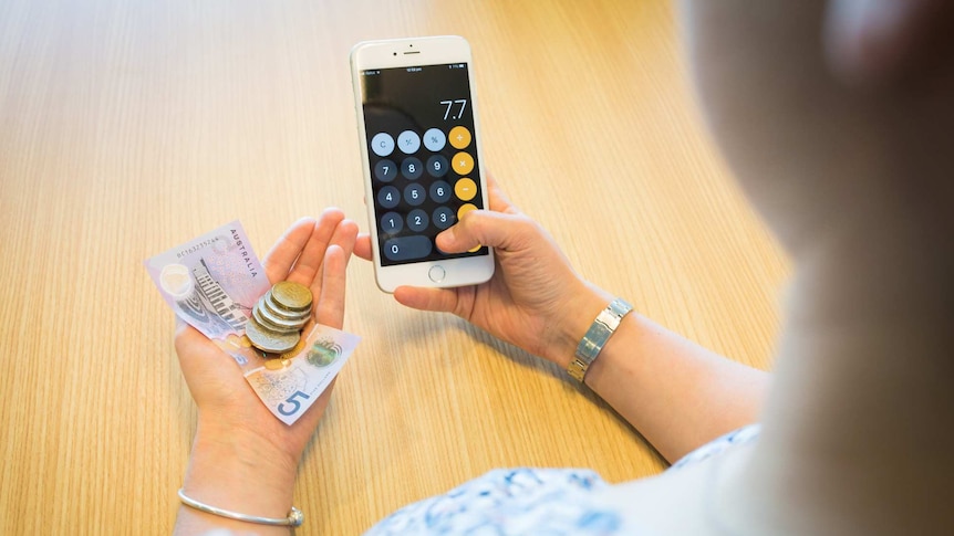 Woman holding a mobile phone and looking at money in her hand.