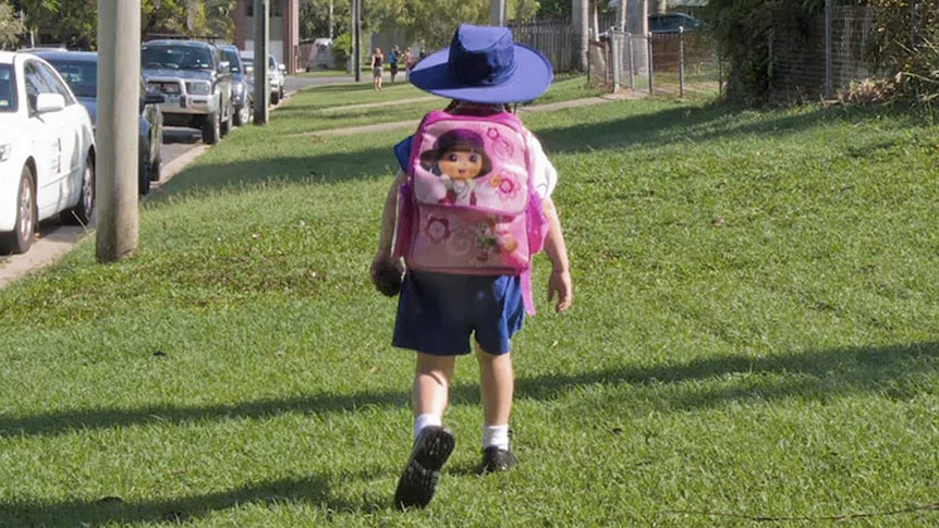 A child walks along grass towards school wearing a large pink backpack