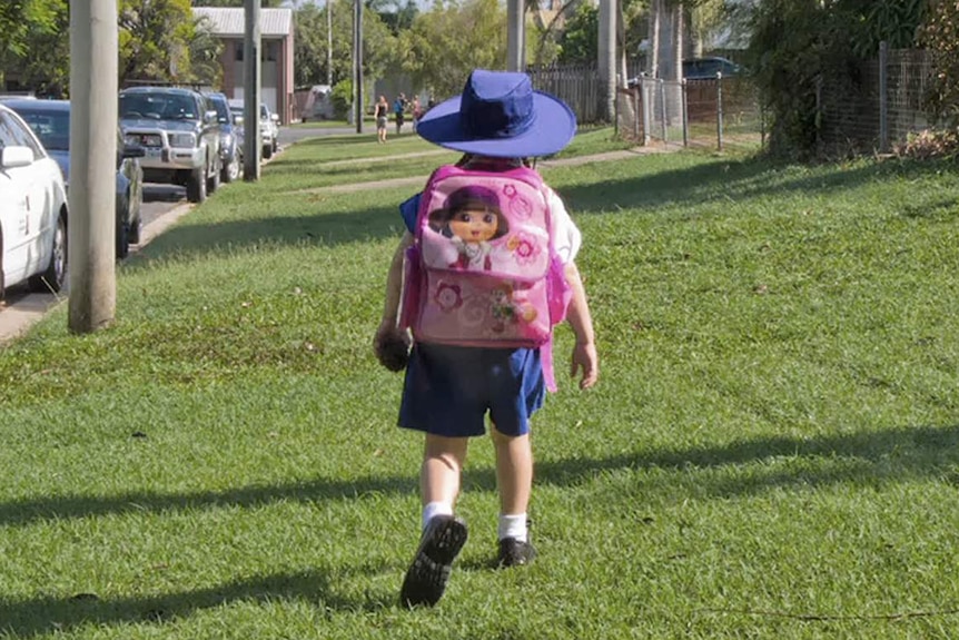 A child walks along grass towards school wearing a large pink backpack