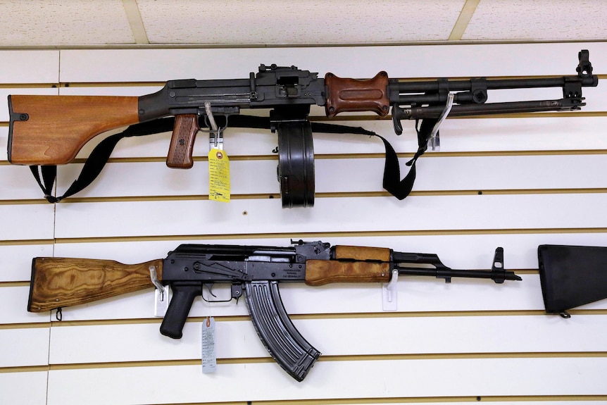 Two assault-style rifles are displayed on a white shop wall with price tags attached.