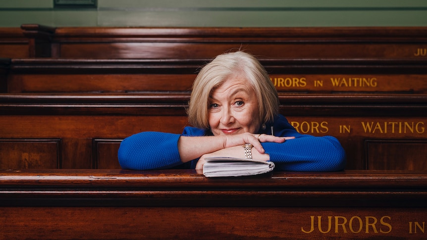 Fair haired woman smiling at camera leaning on court room bench with notepad