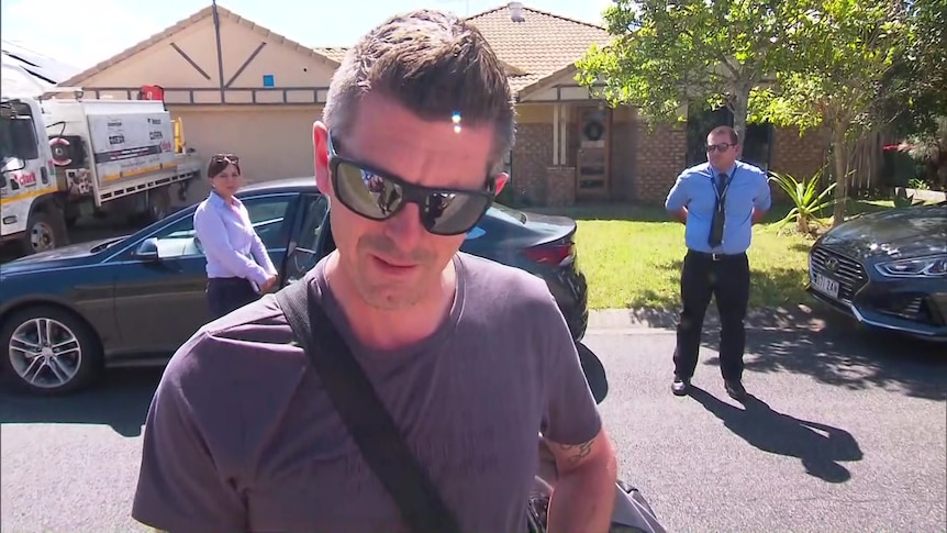 a man in a t-shirt and dark glasses, with two police officers behind him