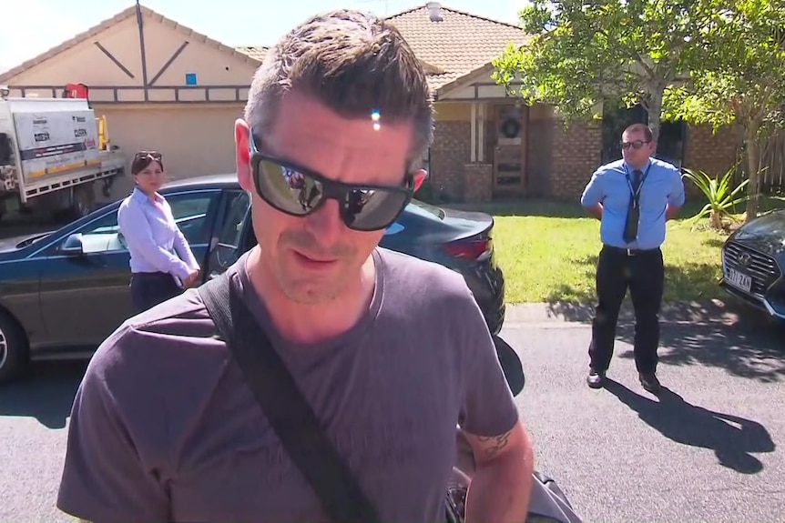 a man in a t-shirt and dark glasses, with two police officers behind him