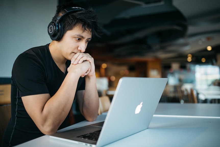 A person sitting at a table looking at a laptop with headphones on