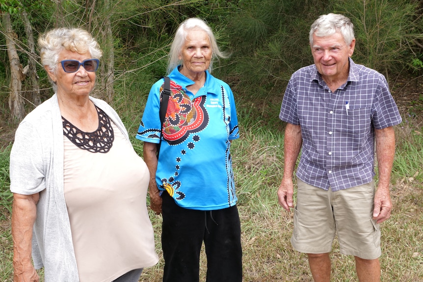 Two elderly Aboriginal women and a man standing together in an open bush location.