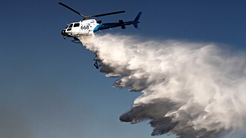 A helicopter drops water on a bushfire.