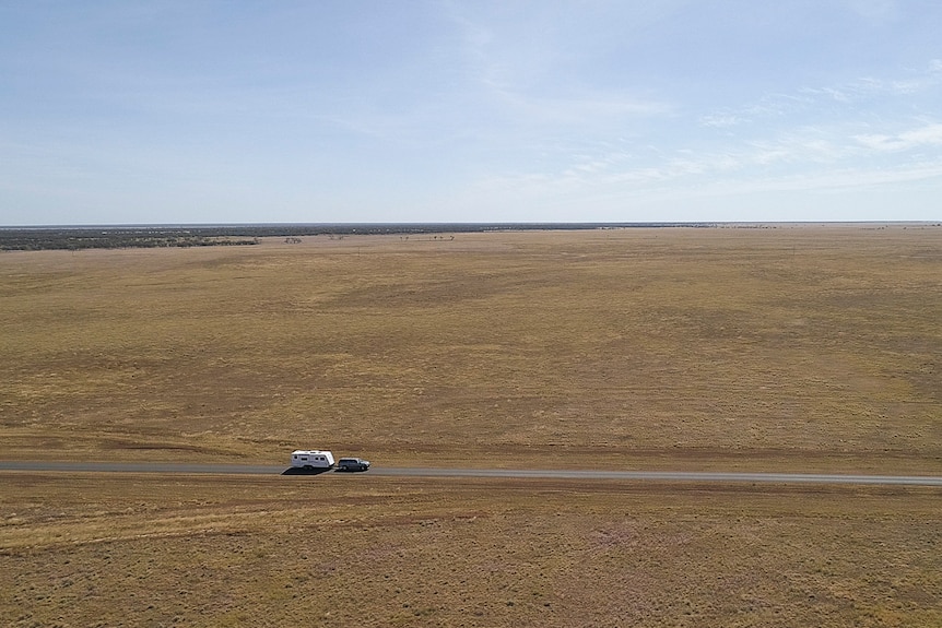 A car towing a caravan across highway in remote western Queensland in July 2019.