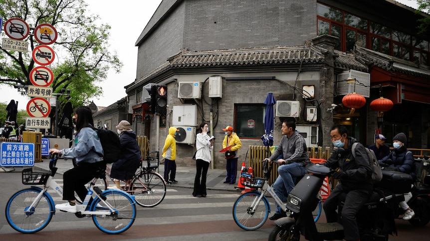 People ride bicycles and scooters on a street during morning rush hour, in Beijing, China.