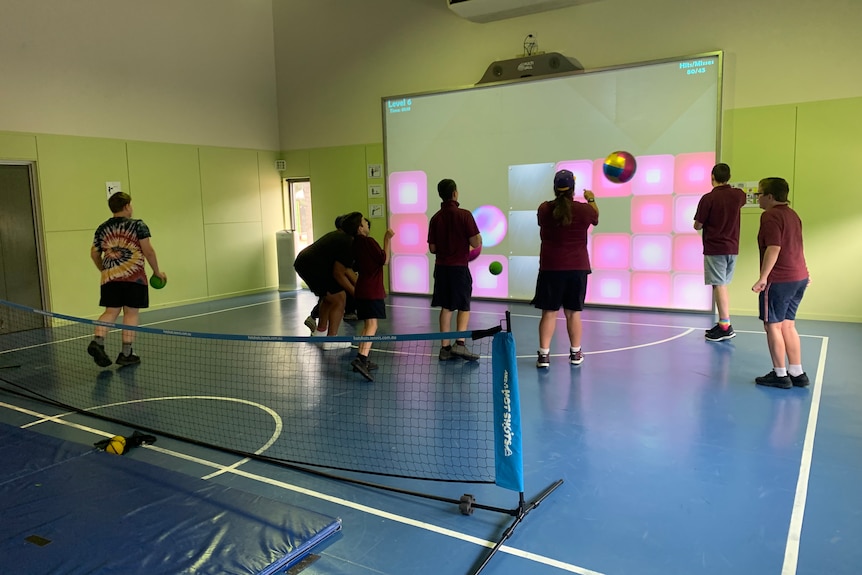 Six young people are playing a game involving a volleyball and an interactive wall that is lit up
