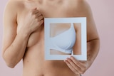 A generic image showing a woman holding up a photo of a breast in a bra to her bare chest.