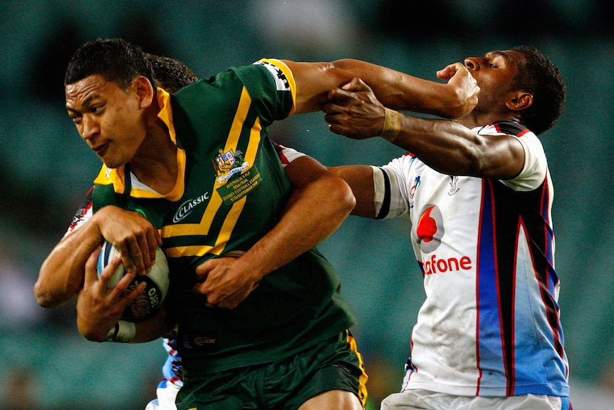 Israel Folau is tackled by two players, one of which he is fending off with his left arm while carrying the ball under his right