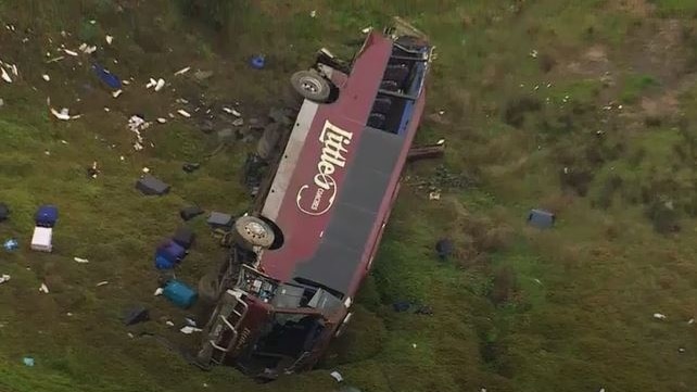 A bus lying on its side at the bottom of a hill with debris strewn for metres.