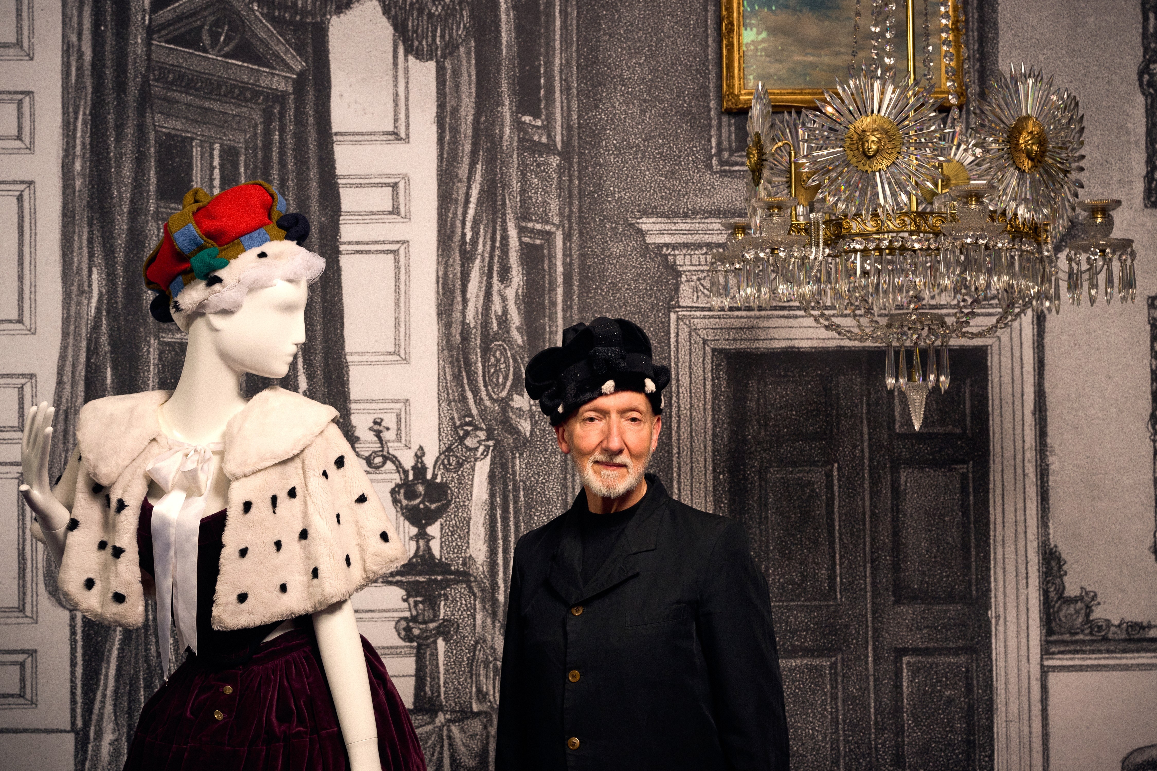 Stephen Jones, con una suave corona de tela negra, está de pie junto a un gran maniquí que lleva una corona de tartán.