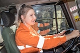 A smiling woman driving a truck inside an open pit gold mine