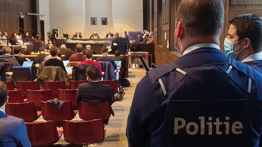 Belgian police officers stand in a courtroom while a verdict is handed down.