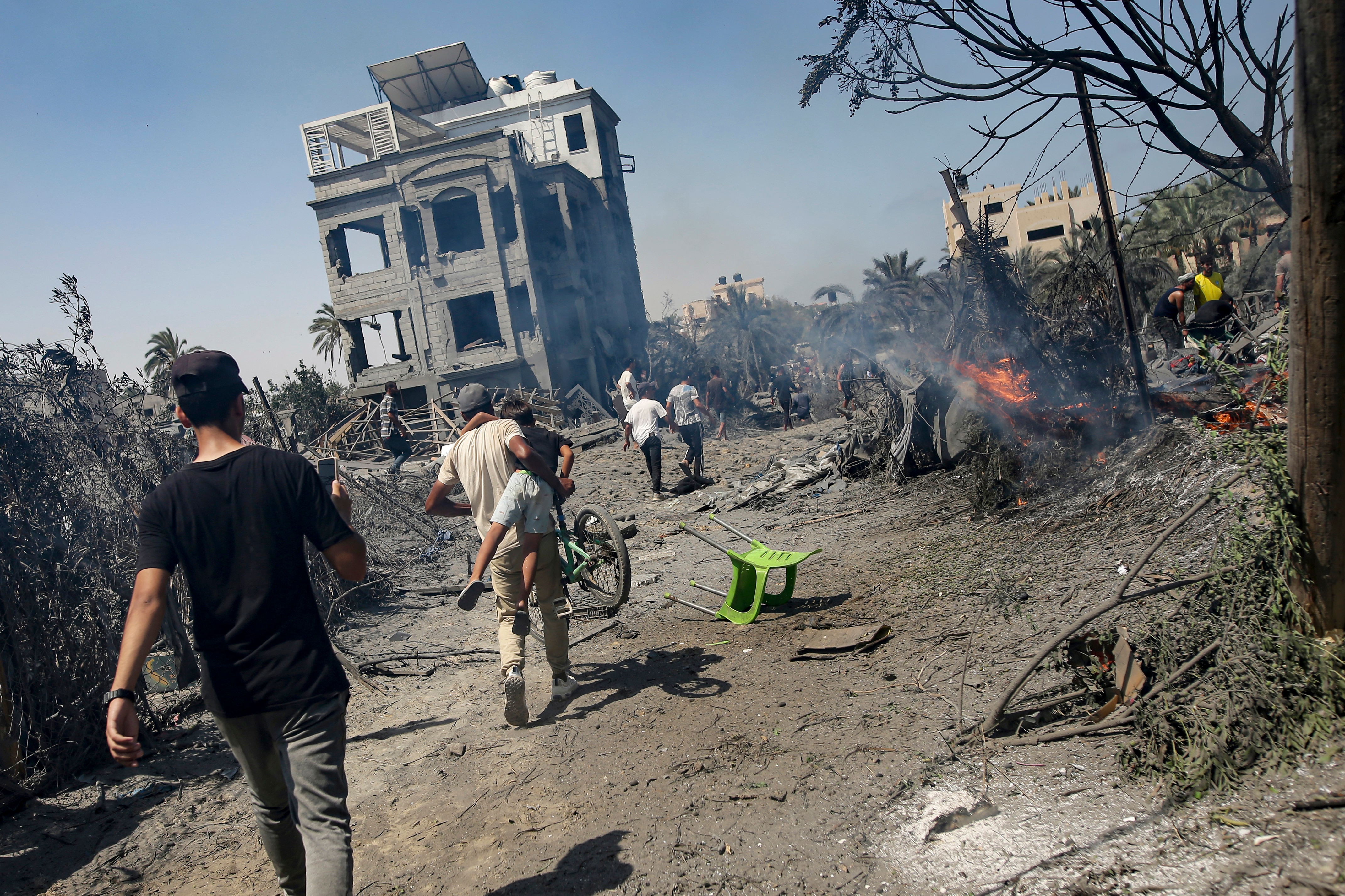 People walk toward a bombed-out building past debris and a small fire