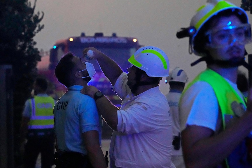 A paramedic washes the eyes of a police officer as a wildfire burns 